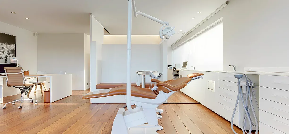 Behandelkamer van Tandpunt Roeselare met een karamelkleurige lederen tandartsstoel, houten vloer en witte kasten.